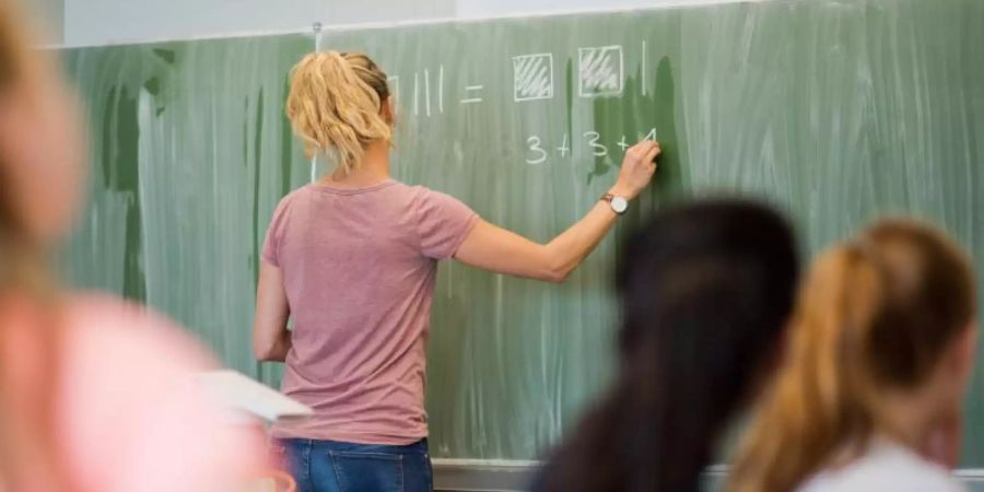 Eine Lehrerin schreibt an eine Schultafel im Mathematikunterricht einer achten Klasse an einer integrierten Gesamtschule.