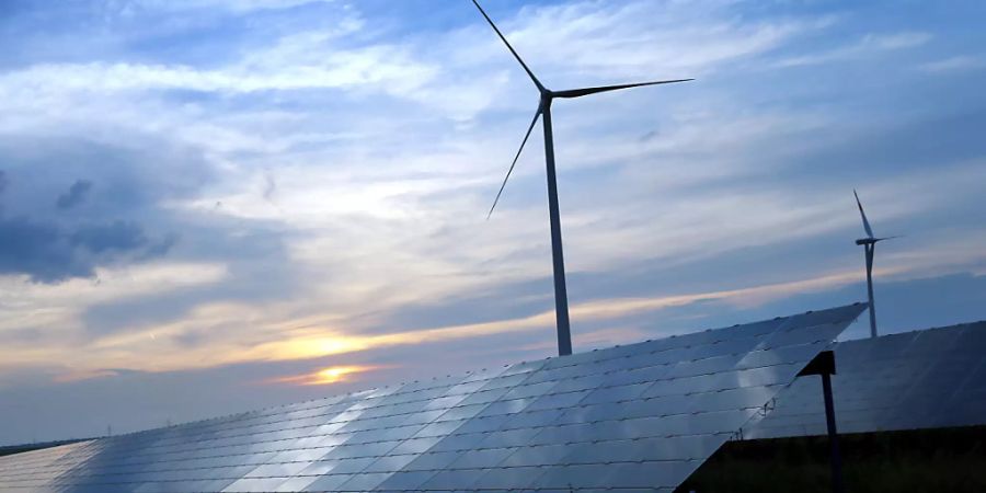 ARCHIV - Der mit Wolken überzogene Abendhimmel spiegelt sich auf den Solarzellen einer vor Windrädern stehenden Solarkraftanlage. Foto: Karl-Josef Hildenbrand/dpa