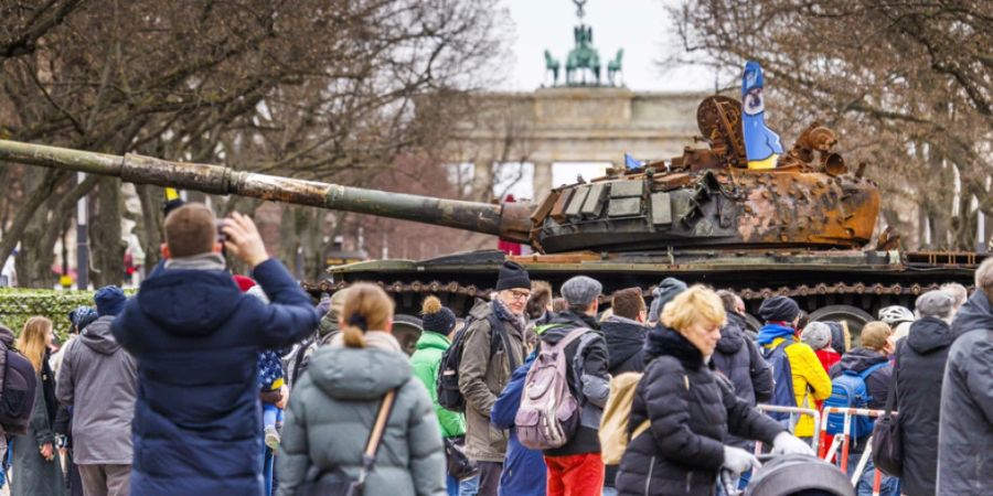 Passanten und Medienvertreter stehen vor einem in der Ukraine zerstörten russischen Panzer. Das Wrack steht auf einem Hänger vor der Botschaft Russlands in Berlin.