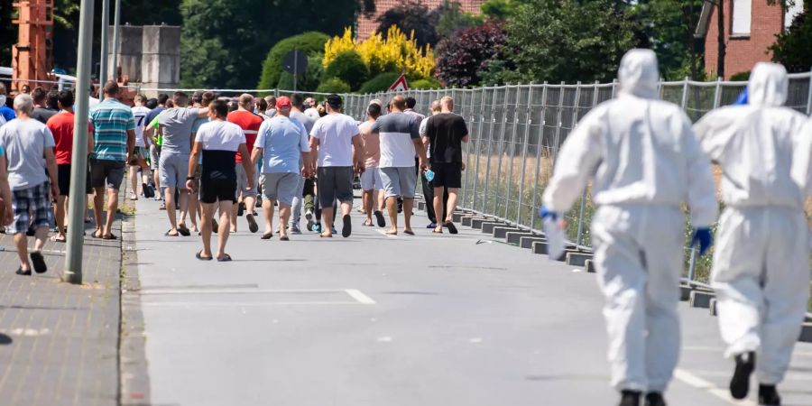 Bewohner der abgesperrten Siedlung in Sürenheide gehen zurück zu ihren Wohnhäusern, gefolgt von Bundeswehr-Soldaten in Schutzanzügen und mit Mund-Nasenschutzmasken, um weitere Personen auf das Coronavirus zu testen. Die Stadt Verl hat nach positiven Corona-Tests bei zahlreichen Tönnies-Mitarbeitern im Stadtteil Sürenheide eine Quarantäne eingerichtet.