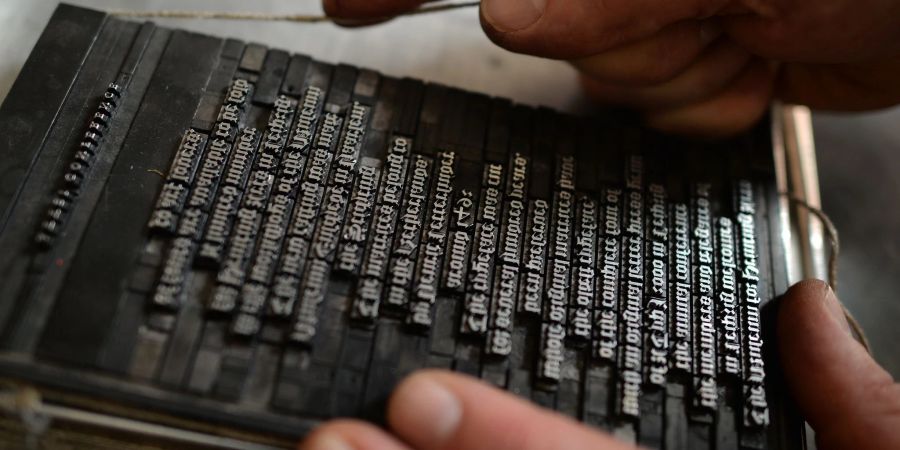 Ein Schriftsetzer des Museums für Druckkunst Leipzig bindet in Leipzig Bleilettern mit einer Kolumnenschnur ein.