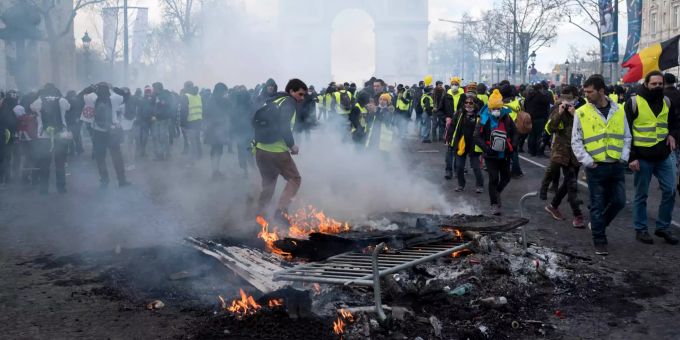 Teilnehmer der Gelbwesten-Proteste gehen auf der Prachtmeile Champs-Élysées an brennenden Gegenständen vorbei. "Gelbwesten"-Proteste in Frankreich