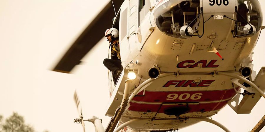 Ein Feuerwehrmann schaut aus einem Hubschrauber heraus, während er an den Löscharbeiten eines Waldbrandes beteiligt ist. Foto: Noah Berger/AP/dpa