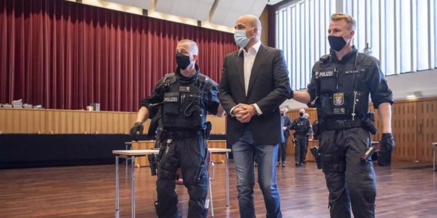 An Händen und Füssen gefesselt ist einer der Hauptangeklagten, den bewaffnete Polizisten in die zu einem Gerichtssaal umfunktionierte Kongresshalle in Giessen bringen. Foto: Boris Roessler/dpa