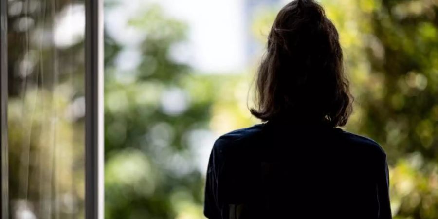 Eine Frau steht in ihrer Wohnung an einem Fenster. (Archivbild). Foto: Fabian Sommer/dpa