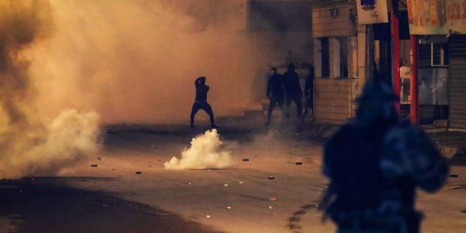 Demonstranten stehen während eines Protestes in Tunis inmitten von Rauchschwaden einer Polizeieinheit gegenüber. tunis protest demonstration polizei