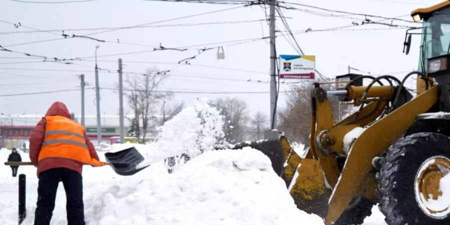 Schnee wegräumen mit schwerem Gerät: Ein Mann schippt Schnee in die Schaufel eines Baggers. Foto: Mihail Tokmakov/SOPA Images via ZUMA Wire/dpa