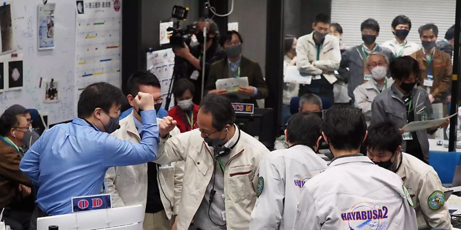 HANDOUT - Die Projektteilnehmer jubeln in einem Kontrollraum des JAXA-Campus Sagamihara, nachdem die erfolgreiche Trennung einer Kapsel vom Raumschiff Hayabusa2 bestätigt wurde. Foto: -/JAXA/AP/dpa