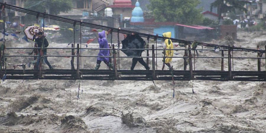 Menschen gehen über eine Brücke, die über den Fluss Beas führt, der aufgrund starker Regenfälle angestiegen ist. Foto: Aqil Khan/AP/dpa