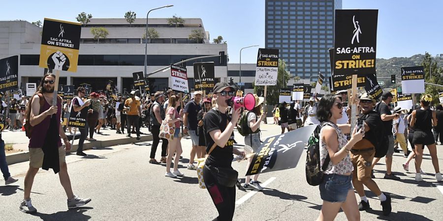 Personen halten Schilder an der Streikpostenkette vor den Universal Studios in Universal City. Der Streik der Schauspieler findet mehr als zwei Monate nach dem Streik der Drehbuchautoren statt, die sich für bessere Bezahlung und Arbeitsbedingungen einsetzen. Foto: Richard Shotwell/Invision/AP/dpa