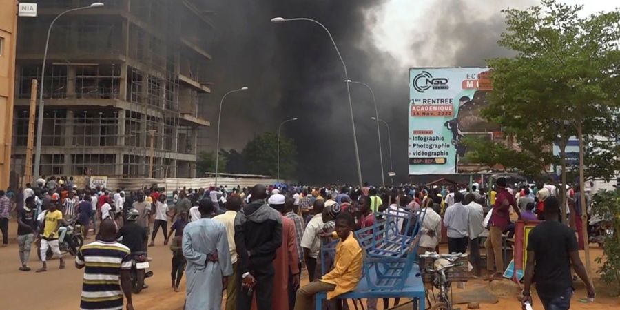 Vor der Kulisse des brennenden Hauptquartiers der Regierungspartei demonstrieren Anhänger meuternder Soldaten in Niamey.