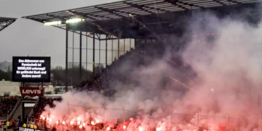 Fans brennen beim Hamburg-Derby zwischen dem FC St. Pauli und dem Hamburger SV Pyrotechnik ab, während eine Anzeigetafel genau davor warnt. Foto: Axel Heimken/dpa