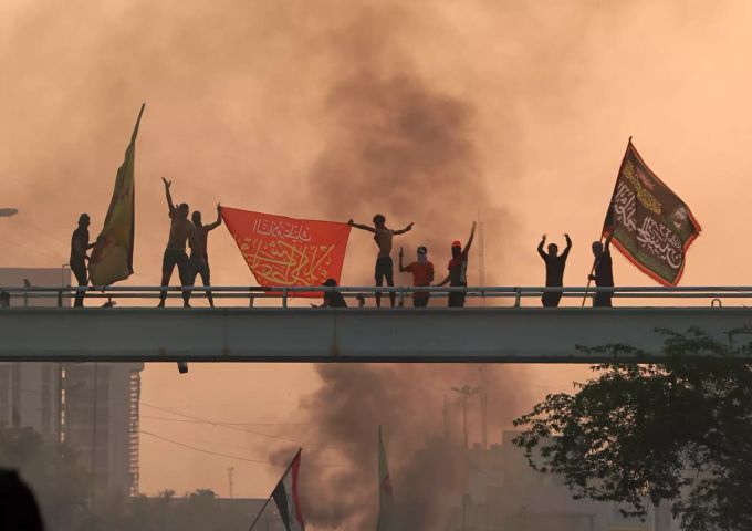 Eine Gruppe Demonstranten schwenken auf einer Brücke Fahnen. Protest in Bagdad
