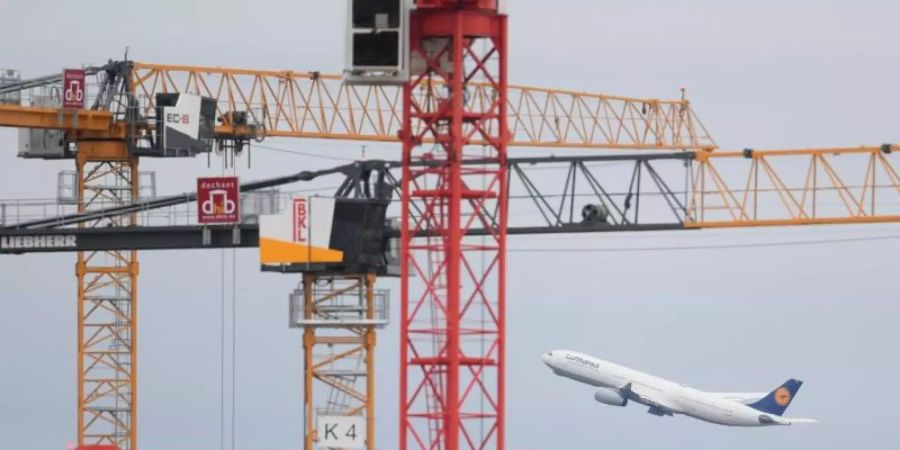 Eine Passagiermaschine der Lufthansa startet auf dem Frankfurter Flughafen hinter Baukränen. Foto: Arne Dedert/dpa/Archivbild