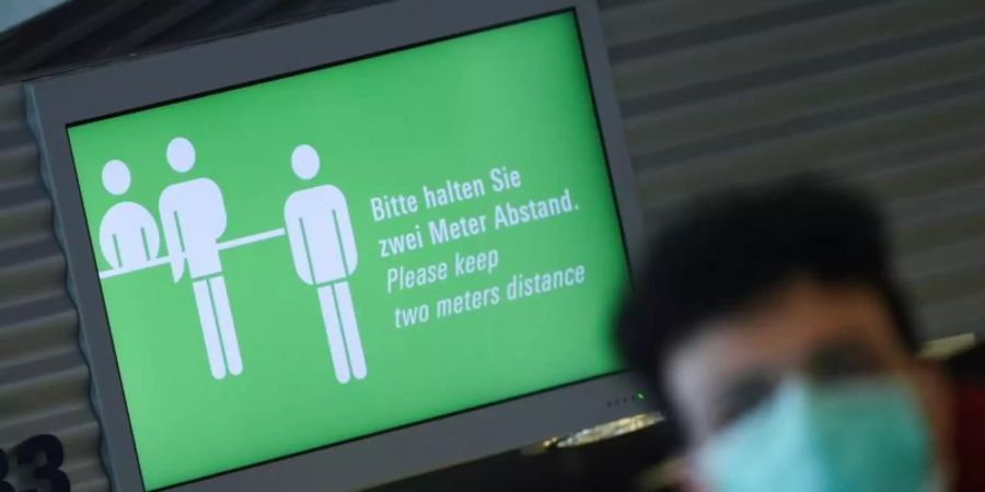 Rückkehrer nach Deutschland werden wohl bald ins Quarantäne müssen. Auf dem Monitor am Frankfurter Flughafen steht: "Bitte halten Sie zwei Meter Abstand!" . Foto: Arne Dedert/dpa