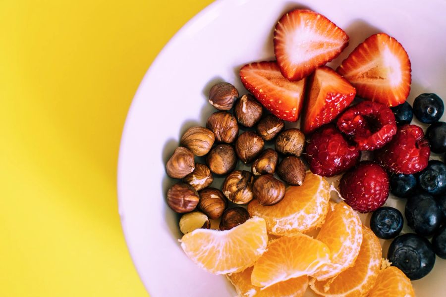 beeren, mandarine und nüsse auf einem teller, gelber hintergrund