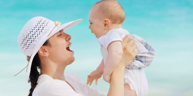 Mutter hebt an einem Strand ihr Baby hoch. Urlaub Kind Mutter