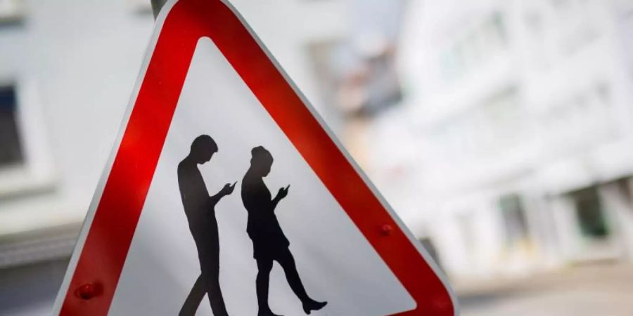 «Smombies» ist ein Kunstwort für Smartphone und Zombie und symbolisiert Menschen, die ständig mit dem Blick auf das Smartphone über die Strassen laufen. Foto: Christoph Schmidt/dpa