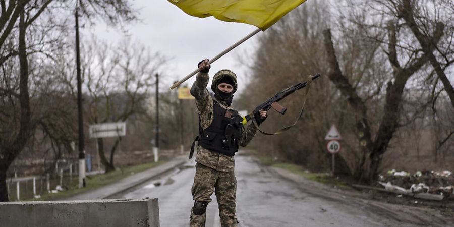 Ein ukrainischer Soldat steht an einer Strassenblockade in Butscha und hält die ukrainische Flagge hoch. Foto: Rodrigo Abd/AP/dpa