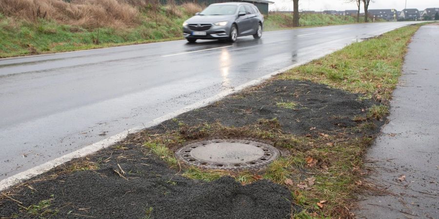 Der Kanaldeckel neben einer Landstrasse in Niederkassel-Lülsdorf, wo ein Passant eine kopfüber steckende Leiche in einem Kanalschacht entdeckt hat.