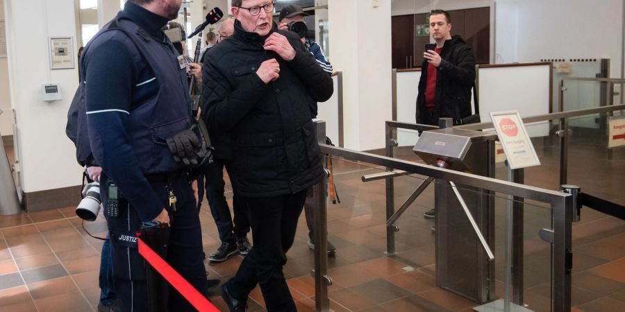 Kardinal Rainer Maria Woelki wird im Foyer des Kölner Landgerichts von einem Justizbeamten (l) zur Sicherheitsschleuse begleitet.