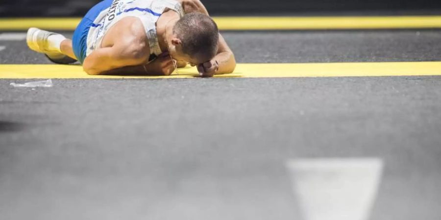 Der italienische Geher Michele Antonelli liegt im Ziel erschöpft auf dem Asphalt. Foto: Oliver Weiken