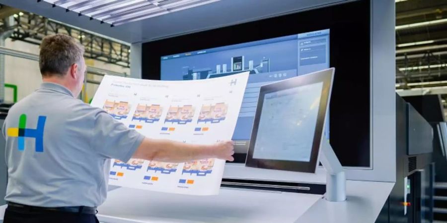 Ein Mitarbeiter hält in einer Werkshalle am Stammsitz der Heidelberger Druckmaschinen AG an einer Digitaldruckmaschine vom Typ «Primefire» einen bedruckten Bogen in den Händen. Foto: Uwe Anspach/dpa
