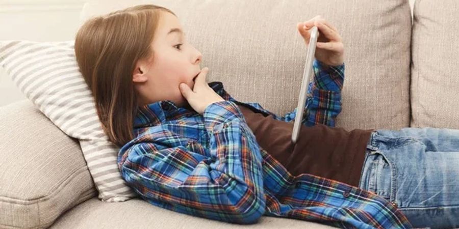 Mädchen sitzt schockiert mit einem Tablet auf dem Sofa.