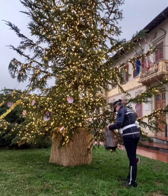HANDOUT - 28.12.2021, Italien, Montemurlo: Ein Polizist entfernt "Hitler-Baumschmuck" vom Gemeinde-Christbaum vor dem Rathaus. Unbekannte hatten rund ein Dutzend rote Papp-Kreise mit Nazi-Abbildungen und dem Gesicht von Adolf Hitler an den Weihnachtsbaum gehangen. Foto: Gemeinde Montemurlo/dpa - ACHTUNG: Nur zur redaktionellen Verwendung im Zusammenhang mit der aktuellen Berichterstattung und nur mit vollständiger Nennung des vorstehenden Credits +++ dpa-Bildfunk +++ Unbekannte hängen Hitler-Christbaumschmuck vor Rathaus auf