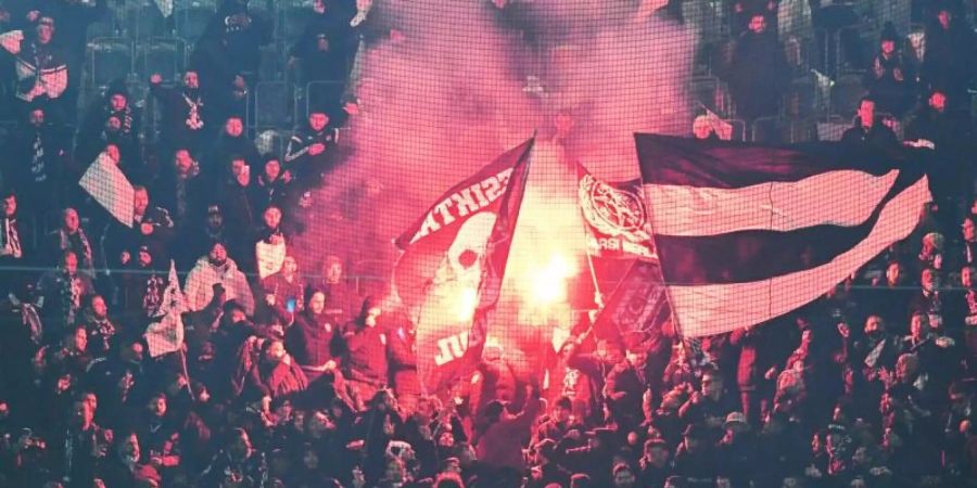 Fans von Besiktas stehen hinter einem Zaun auf der Tribüne und zünden Pyrotechnik. Foto: Bernd Thissen/dpa