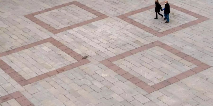 Passanten laufen über den fast leeren Marienplatz vor dem Rathaus in der Innenstadt von München. Foto: Peter Kneffel/dpa