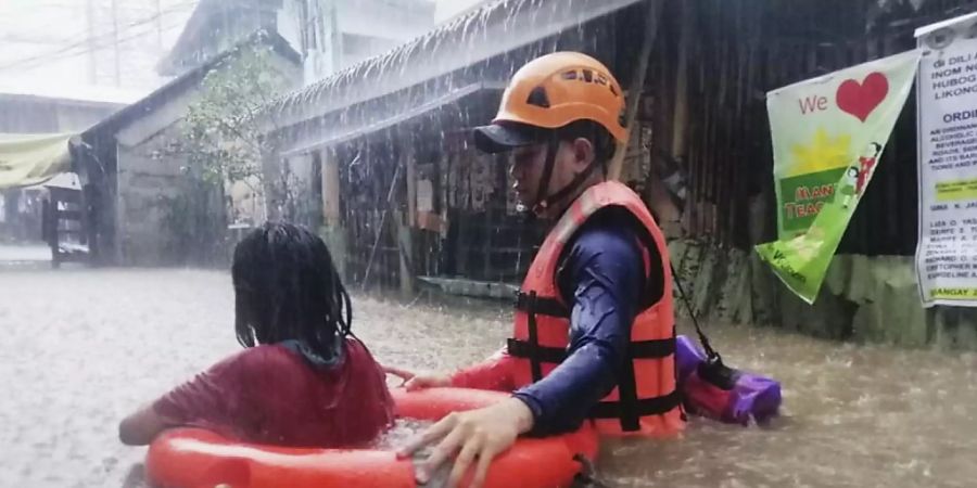 HANDOUT - Dieses von der philippinischen Küstenwache zur Verfügung gestellte Foto zeigt eine Rettungskraft die ein Mädchen durch das Hochwasser evakuiert. Foto: Uncredited/Philippine Coast Guard/dpa - ACHTUNG: Nur zur redaktionellen Verwendung und nur mit vollständiger Nennung des vorstehenden Credits