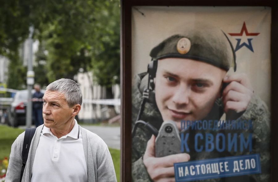 Ein Mann vor einem Plakat in Russland, welches Soldaten für den Ukraine Krieg aufruft.