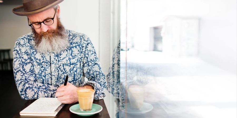 älterer mann schreibt liste, blaues hemd, café