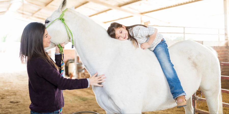 Mädchen auf einem weissen Pferd in der Therapie.