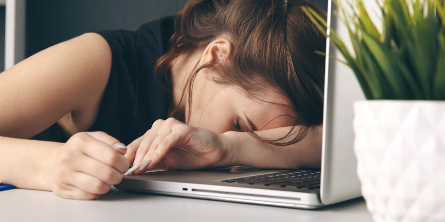 Frau liegt mit ihrem Gesicht erschöpft auf dem Laptop