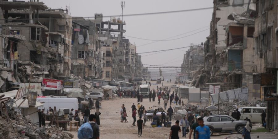 ARCHIV - Palästinenser gehen in der Stadt Gaza eine Straße entlang, die von zerstörten Gebäuden umgeben ist. Foto: Abdel Kareem Hana/AP/dpa/Archivbild