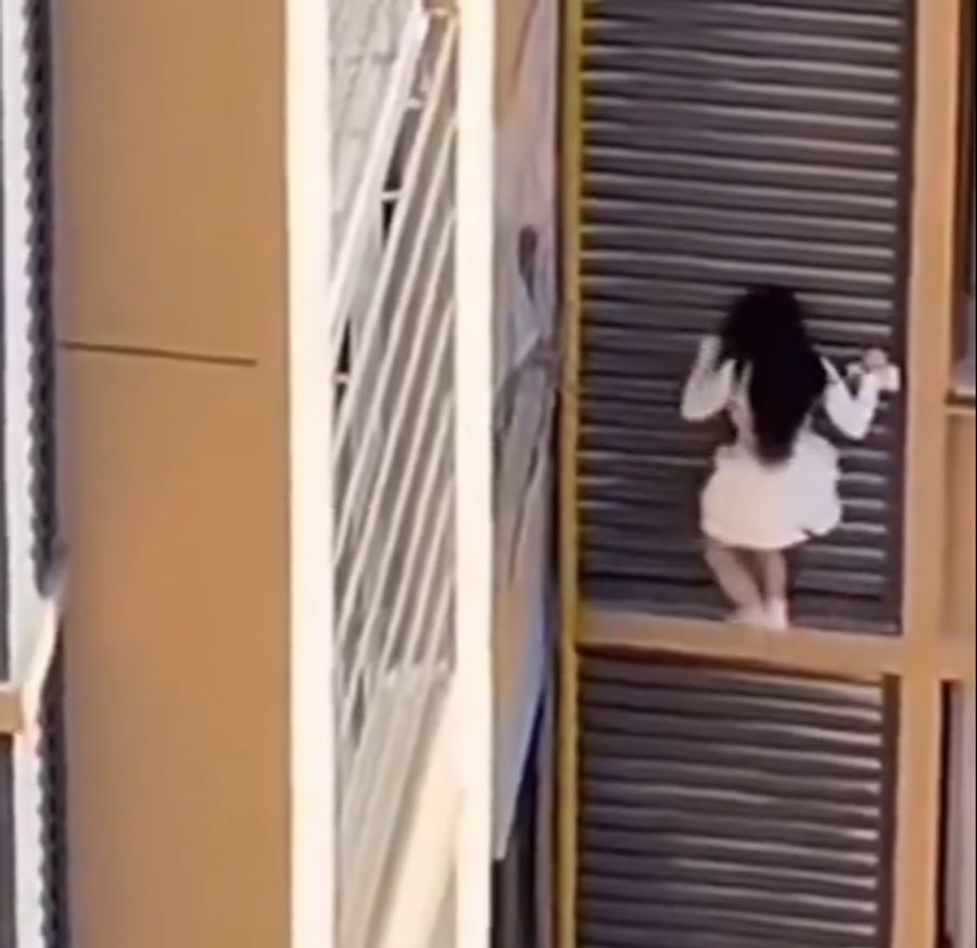 Flink und nur in Socken hangelt sich die Frau an der Fassade entlang.