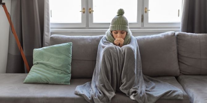 Frau mit Mütze, Schal und Decke auf einem Sofa