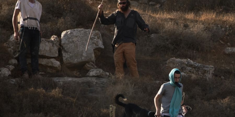 ARCHIV - Israelische Siedler gehen einen Hügel hinunter, während israelische Soldaten den Zugang für Palästinenser zu einem Gebiet für die Olivenernte im Westjordanlanddorf Sa'ir i...