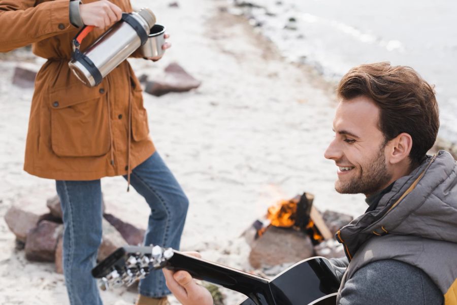 mann, gitarre-spielend am strand, frau giesst tee in thermos-kanne