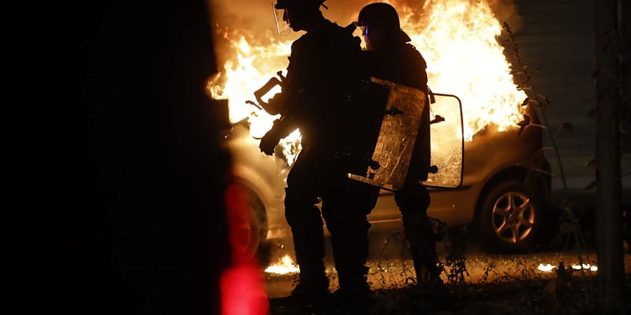 Bereitschaftspolizisten stehen am 30. Juni in der Nähe eines brennenden Autos in Strassburg. Foto: Jean-Francois Badias/AP/dpa