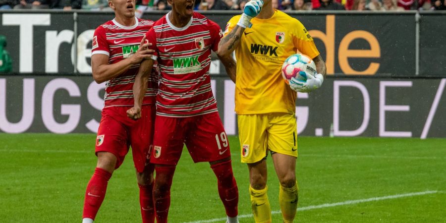 Augsburgs Torwart Rafal Gikiewicz (r) lässt sich nach dem gehaltenen Elfmeter von Emirdan Demirovic (l) und Felix Uduokhai feiern.