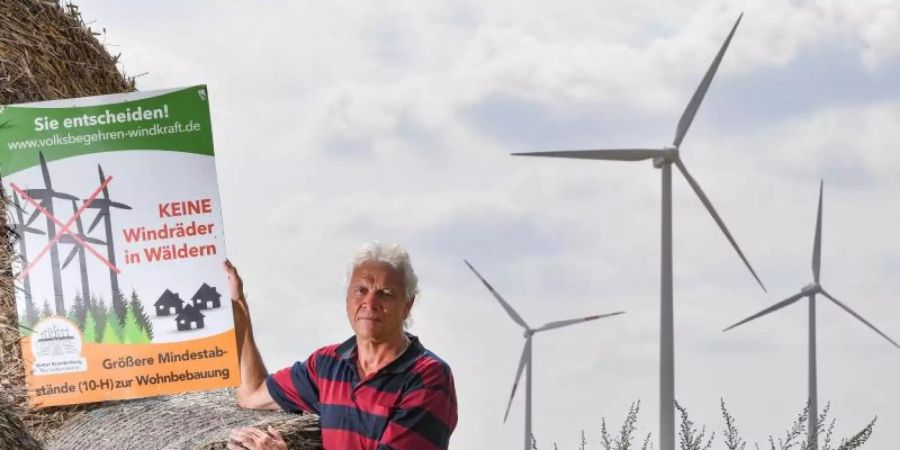 Rainer Ebeling, Sprecher der Bürgerinitiative in Crussow, einem Ortsteil von Angermünde in der Uckermark, steht mit einem Protestplakat auf einem Feld mit Windrädern. Foto: Patrick Pleul