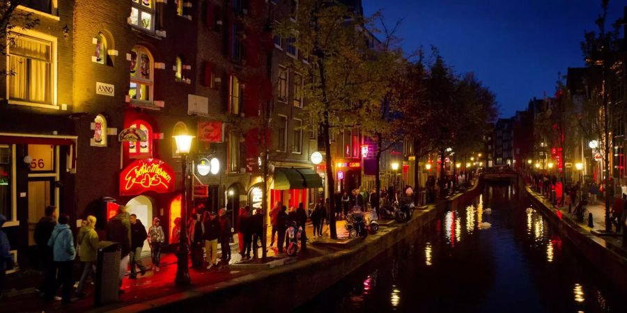 Menschen schlendern am Abend an einer Gracht entlang durch den Rotlichtbezirk De Wallen in Amsterdam.