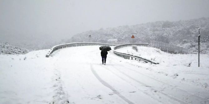 Eine Frau läuft auf einer schneebedeckten Strasse in Griechenland.