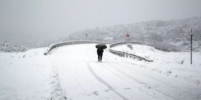 Räumfahrzeuge konnten nur mühsam die Fahrbahn der wichtigen Nord-Süd-Verkehrsachse Griechenlands vom Schnee frei halten. Eine Frau läuft auf einer schneebedeckten Strasse in Griechenland.