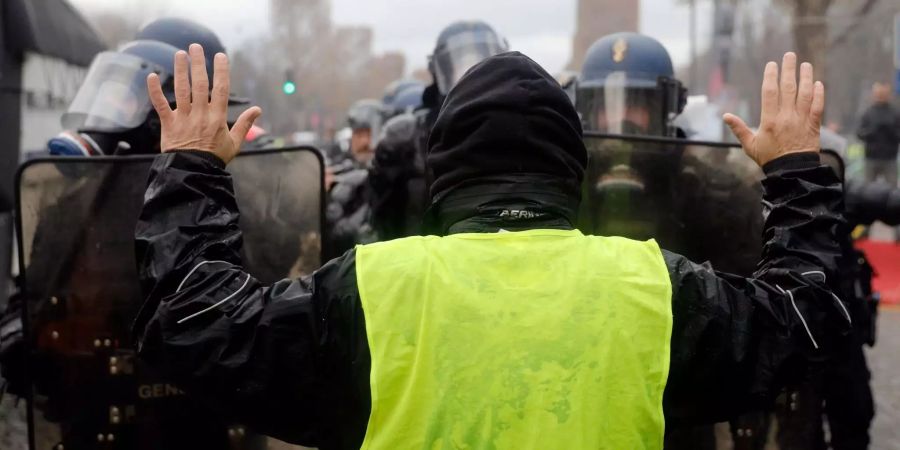 Ein Demonstrant steht mit erhobenen Händen vor einer Blockade von Polizisten auf der Champs-Elysees-Allee.