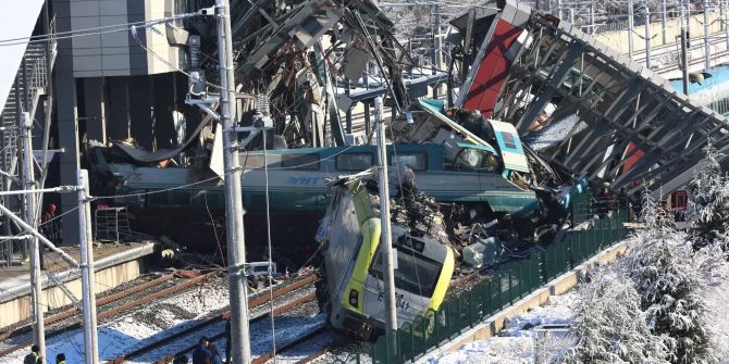 Mehrere beschädigte und entgleiste Wagons und eine Lokomotive liegen unter den trümmern eines Bahnhofs in Ankara im Gleisbett.