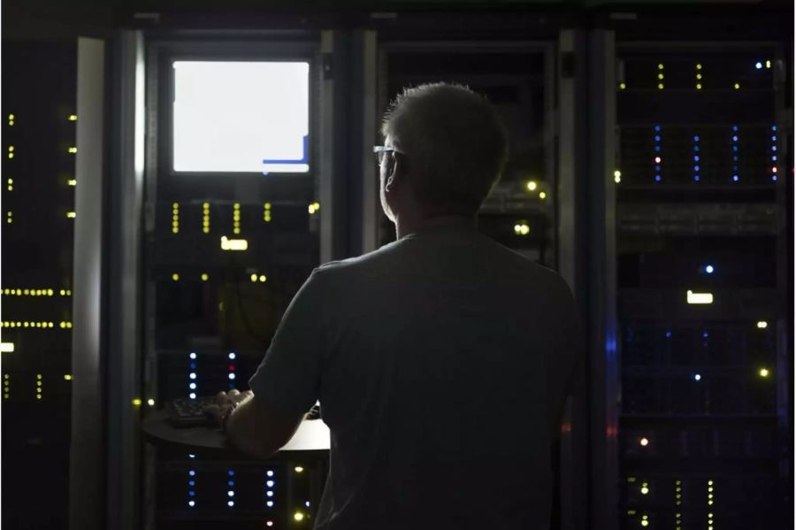 Mann mit Brille vor einem hellen Bildschirm in einem Serverraum - Keystone